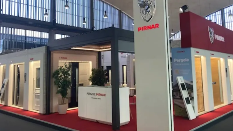 Na razstavi so prikazane različne vrata in pergole, razporejene ob steni.