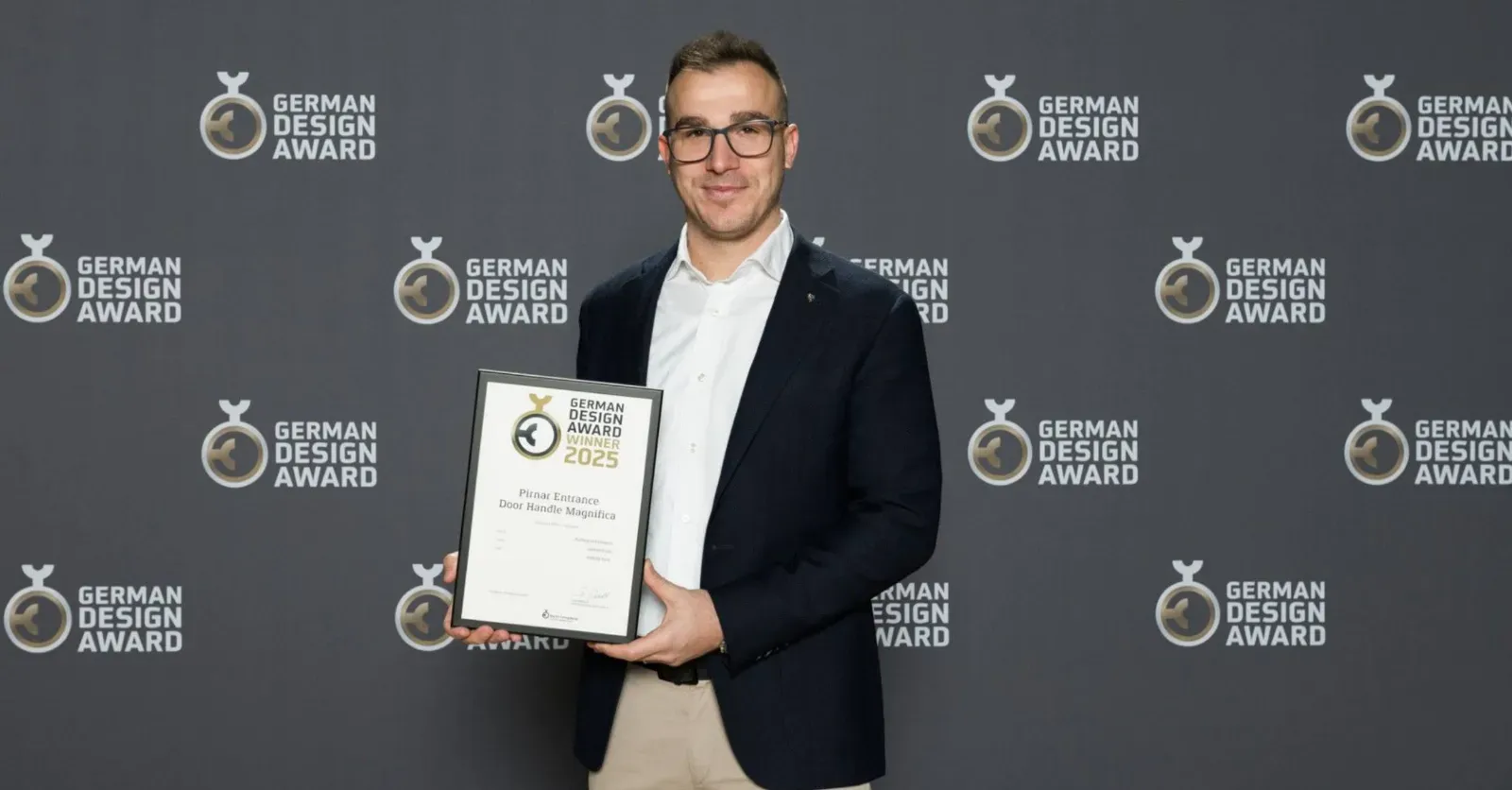 Moški drži priznanje za oblikovanje pred ozadjem z logotipi German Design Award.