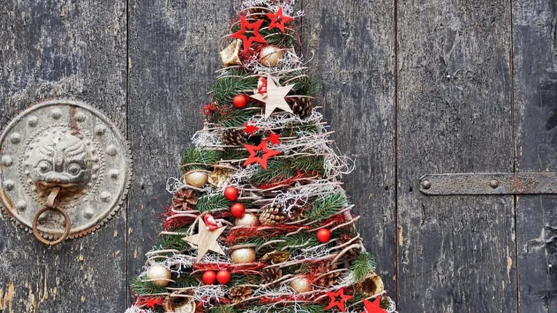 Na črnih lesenih vratih je okrogla kovinska kljuka in božično drevo iz naravnih materialov ter okraskov.