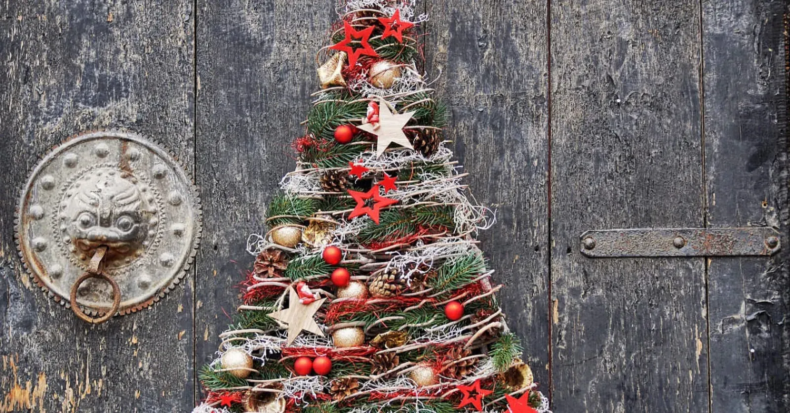 Na črnih lesenih vratih je okrogla kovinska kljuka in božično drevo iz naravnih materialov ter okraskov.