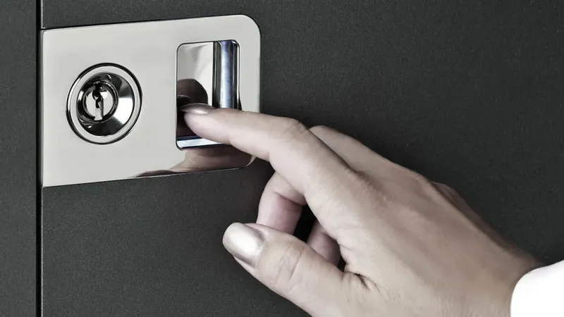 Na črni površini je ključavnica in gumb za odklepanje, na katerega se dotika prst.