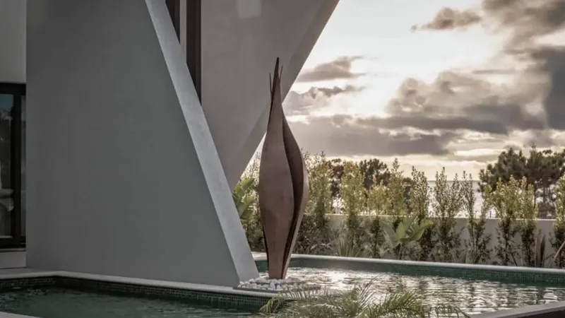 Pergola iz betona s kovinsko skulpturo ob bazenu in zelenjem v ozadju.