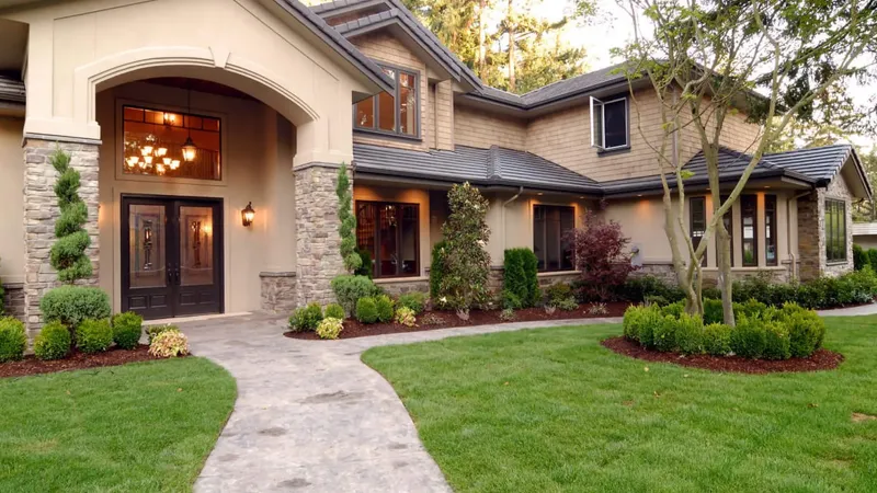 Dve leseni vhodni vrata z okni in svetilkami, obkrožena z zelenjem in tlakovanjem.