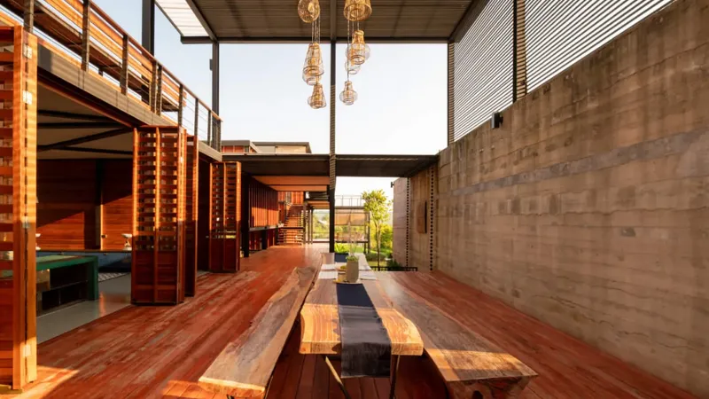 Lesena pergola s visečimi svetili in dolga lesena miza s prtom v središču prostora.