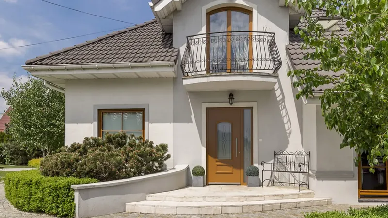 Vhodna vrata so rjava z steklenim delom in okrasno obrobo, obdanimi z dvema okrasnima lončnicama.