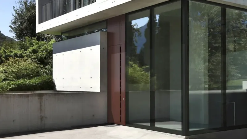 Steklena vrata so nameščena ob betonski steni, obdanih z zelenjem.