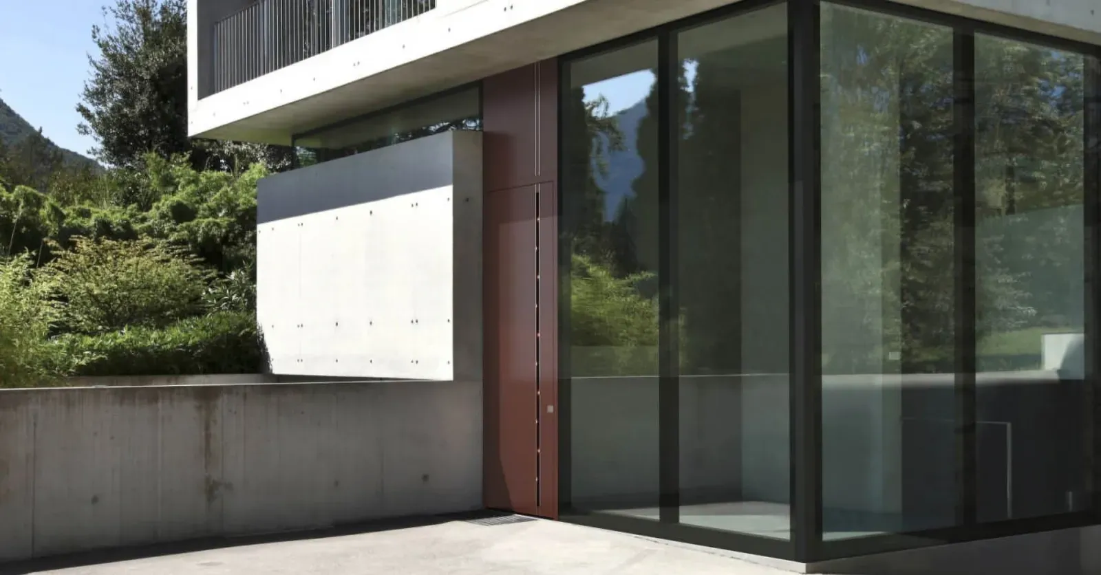 Steklena vrata so nameščena ob betonski steni, obdanih z zelenjem.