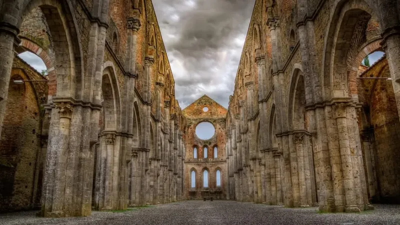 Ruševine z visokimi kamnitimi stebri in obokanimi odprtinami, ki vodijo do okroglega okna na koncu.