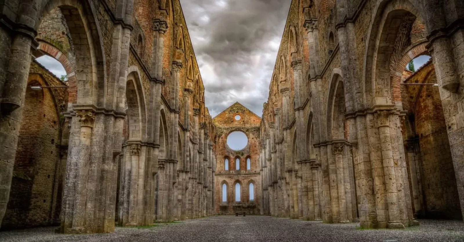 Ruševine z visokimi kamnitimi stebri in obokanimi odprtinami, ki vodijo do okroglega okna na koncu.