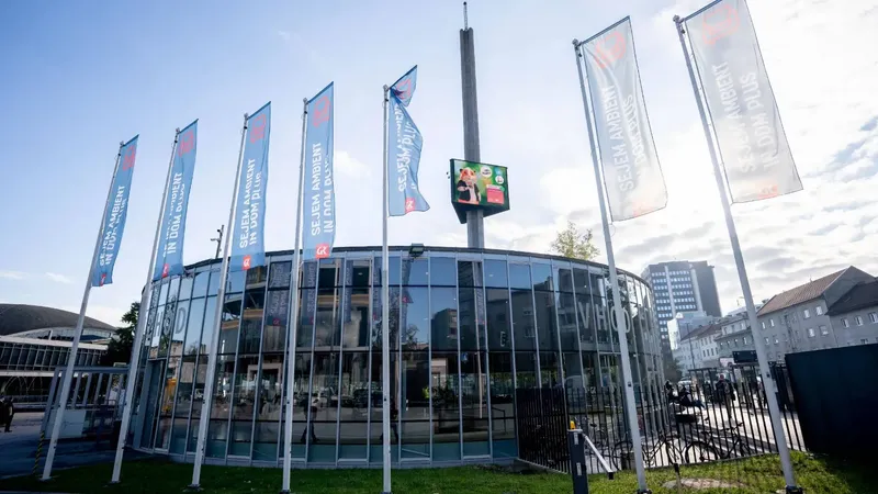 Stekleno vhodno vrata z večjimi steklenimi paneli in visokimi zastavami ob strani.