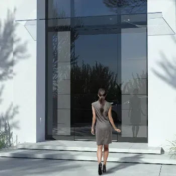 Ženska stoji pred velikimi steklenimi vrati z nadstreškom.