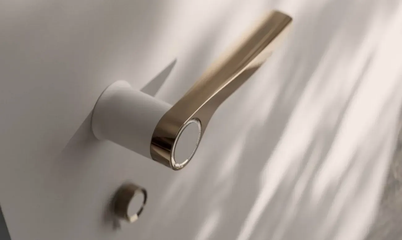 Ročaj bele barve z zlatim detajlom na vratih z okroglo ključavnico.