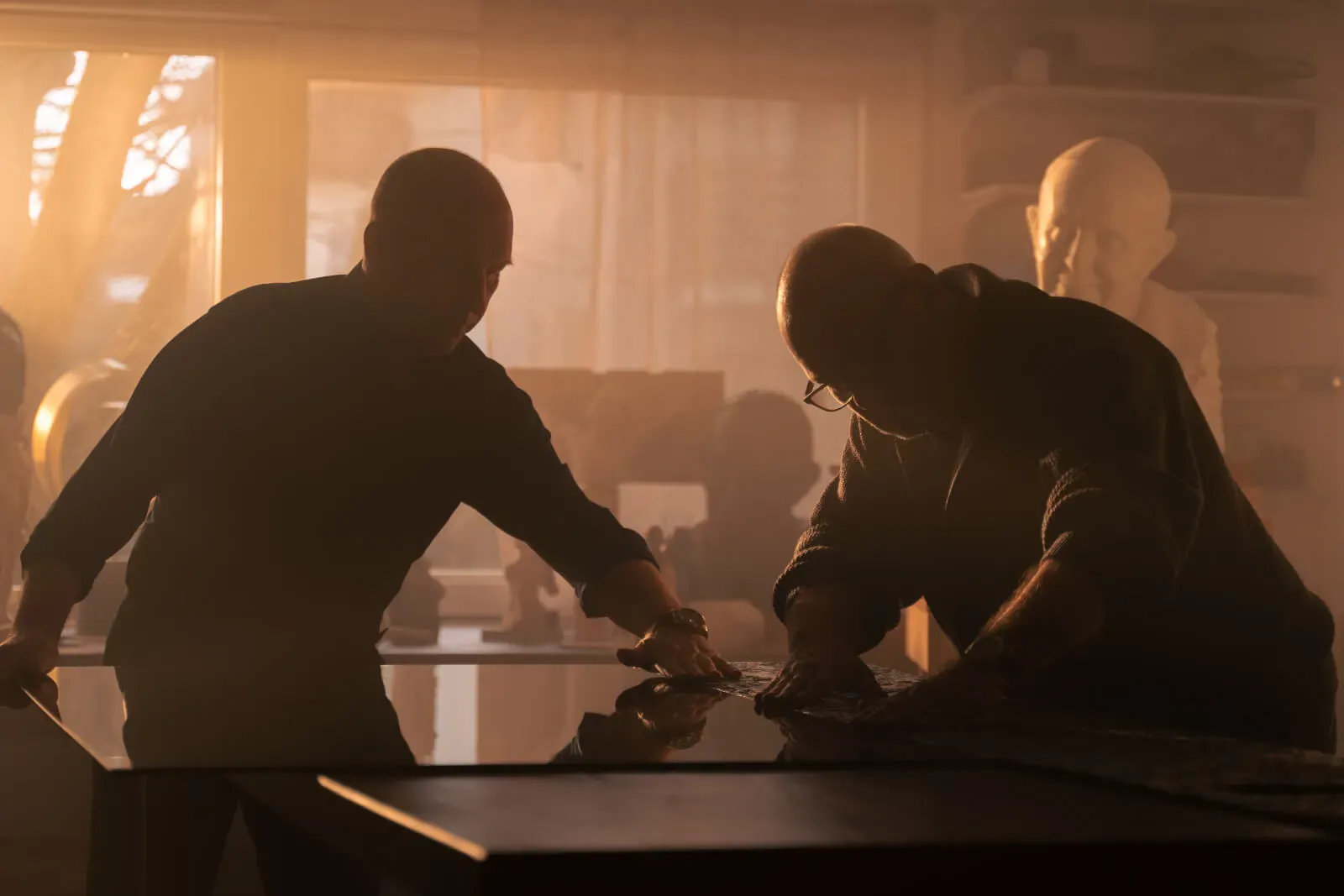 Dva moška delata na mizi, medtem ko je v ozadju vidna svetloba skozi okno.